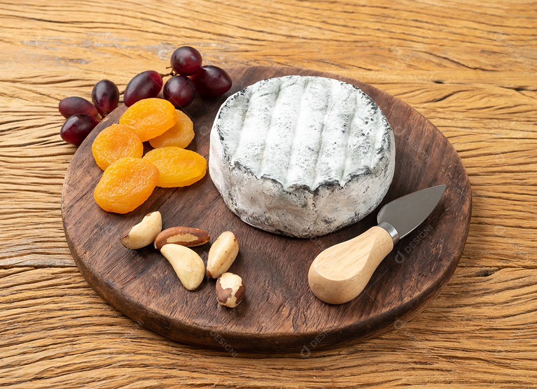 Queijo artesanal brasileiro com frutas e nozes sobre mesa de madeira.