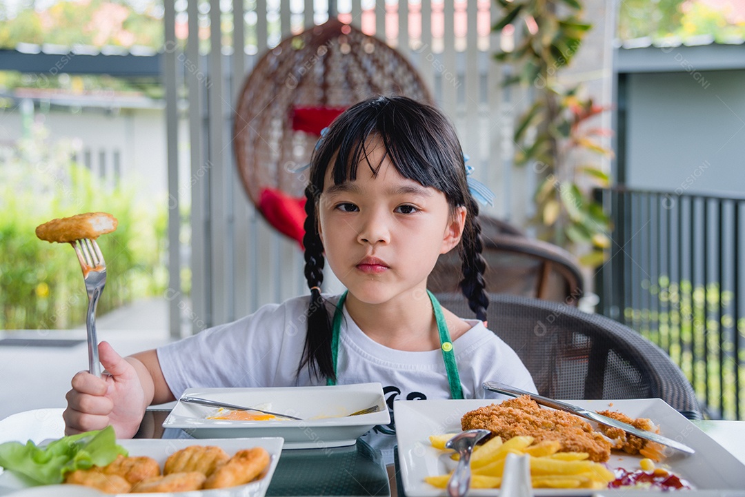 Menina asiática comendo nuggets de frango fast-food na mesa.