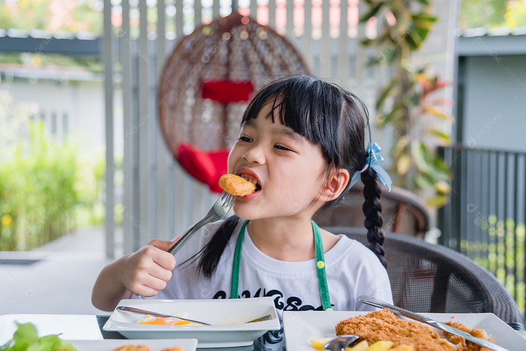 Menina asiática comendo nuggets de frango fast-food na mesa.