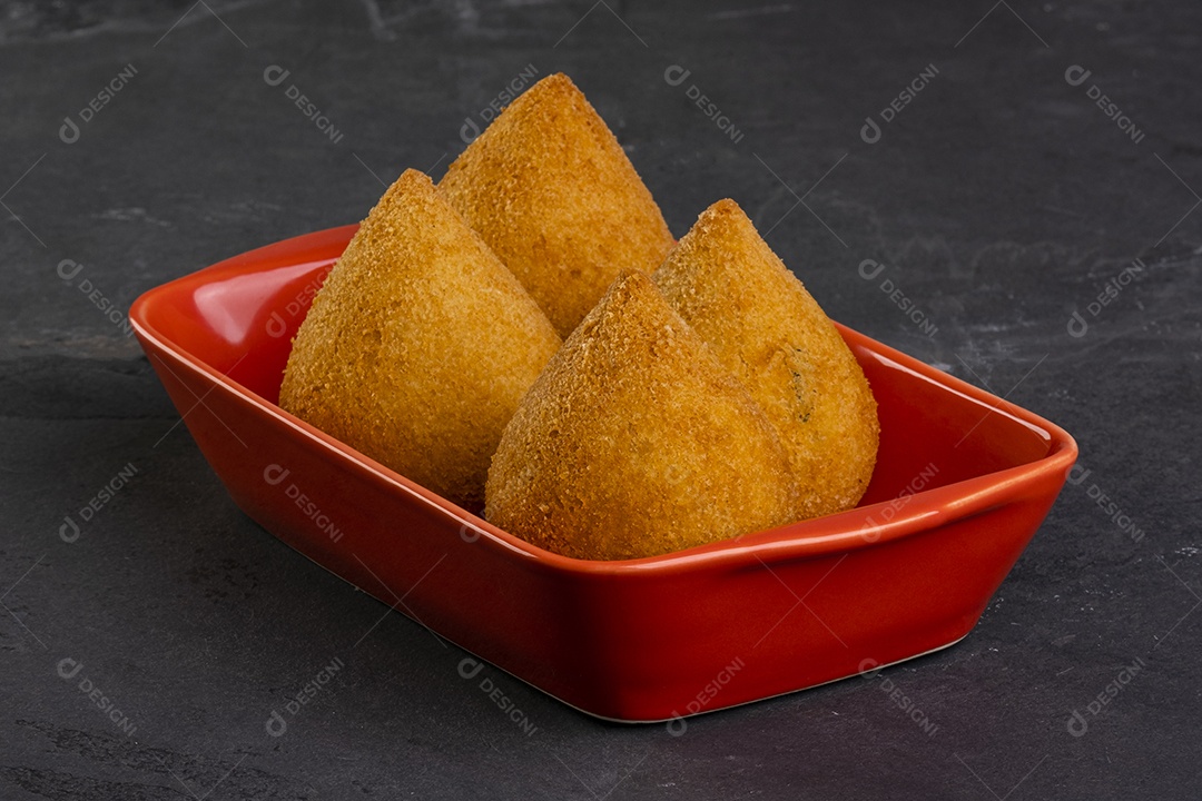 Coxinha frita tradicional em um recipiente vermelho em uma pedra de ardósia.