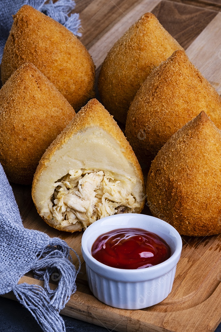 Coxinhas fritas tradicionais em uma tábua de madeira e uma panela de ketchup.