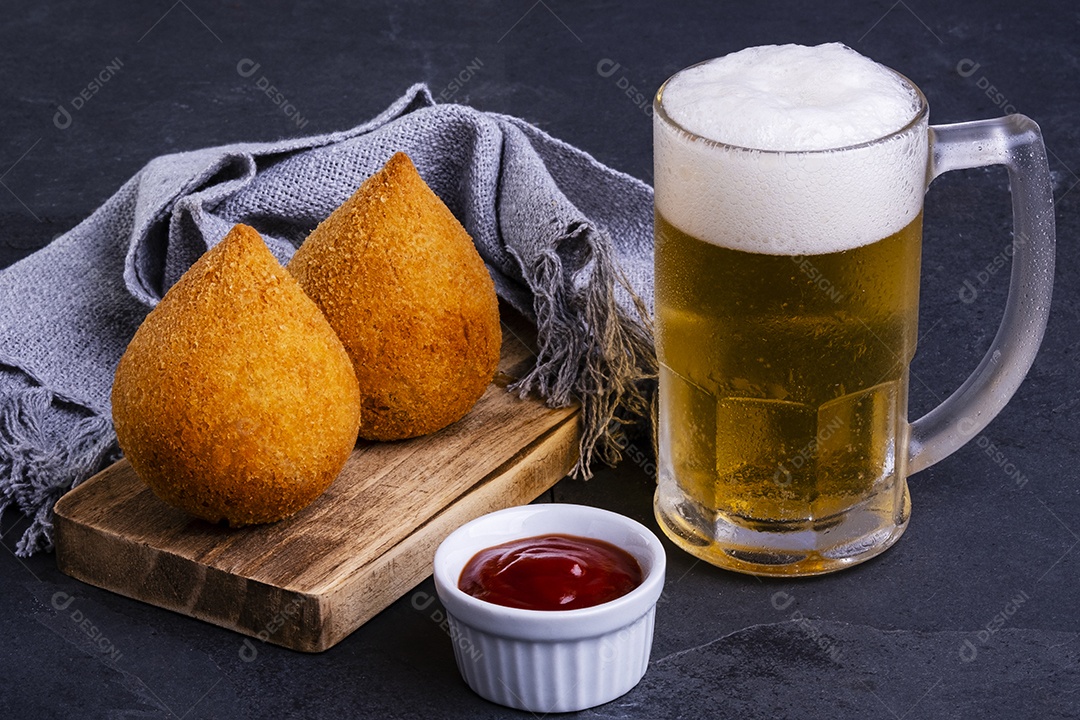 Tradicional coxinha frita recheada com frango e caneca de cerveja gelada.