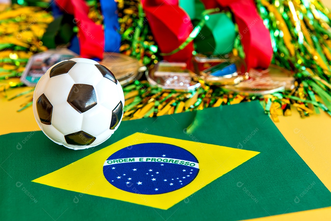 Bola de futebol, medalha e bandeira brasileira em fundo amarelo