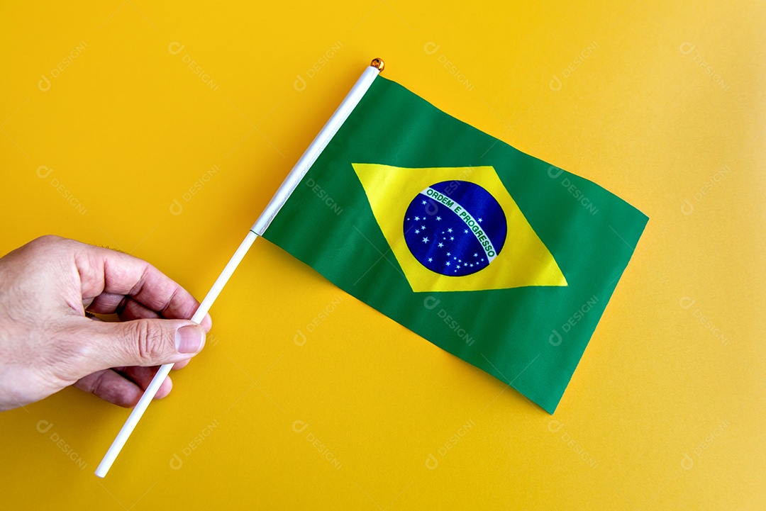 Mãos segurando a bandeira brasileira em um fundo amarelo