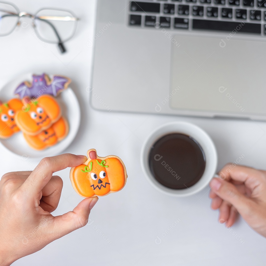 Mão segurando biscoito de abóbora de Halloween e tomando café