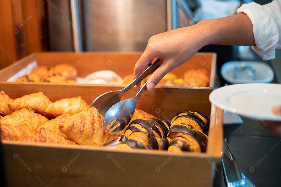 Mãos do homem segurando pão com pinças em uma loja de pão, croissants