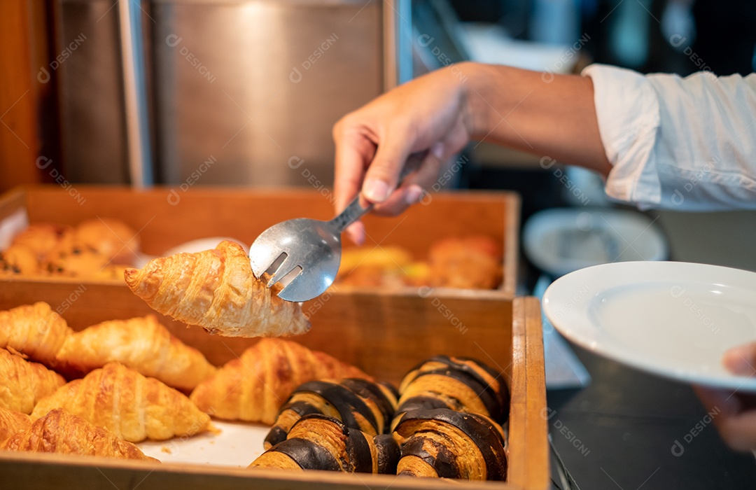Mãos do homem segurando pão com pinças em uma loja de pão, croissants