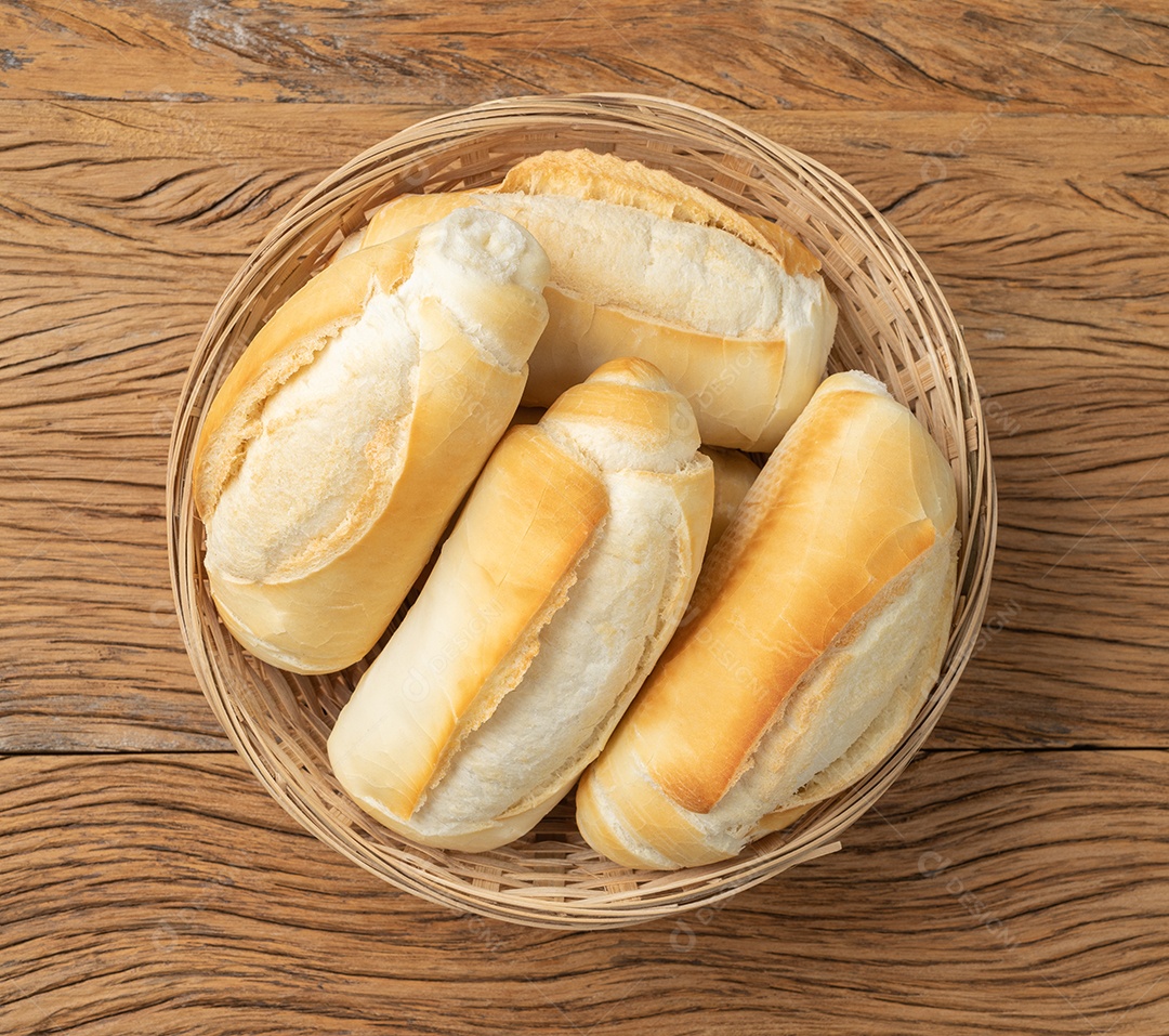 Pão francês, pão de sal ou pistolet em uma cesta sobre a mesa de madeira.
