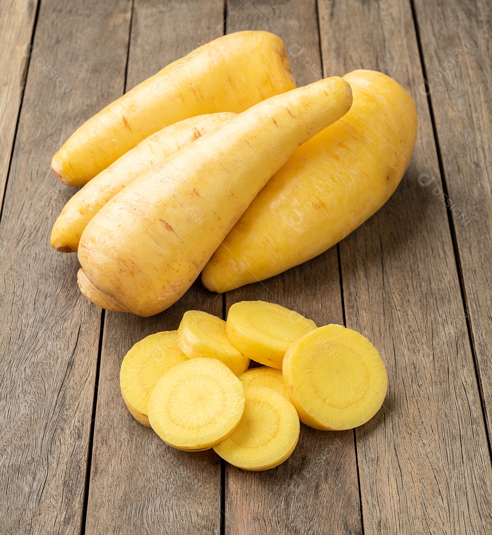 Mandioquinha crua ou arracacha com fatias sobre mesa de madeira.