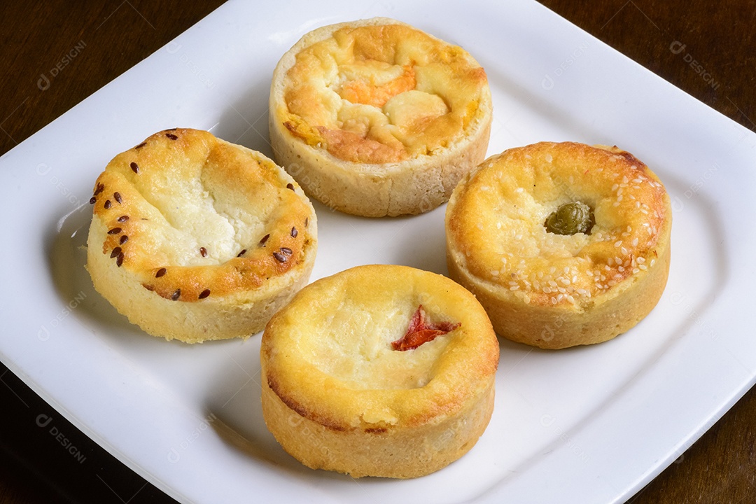 Mini quiches petiscos de sabores variados em um prato branco.
