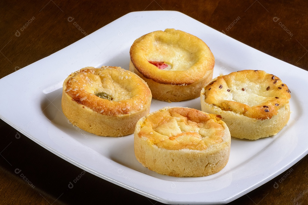 Mini quiches petiscos de sabores variados em um prato branco.