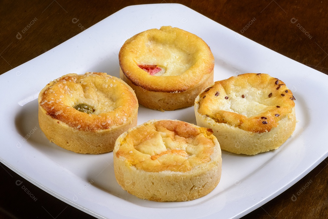 Mini quiches petiscos de sabores variados em um prato branco.