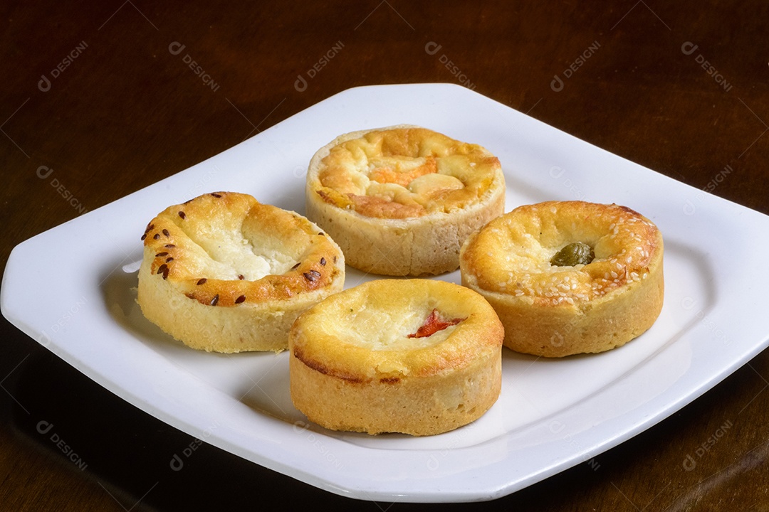 Mini quiches petiscos de sabores variados em um prato branco.