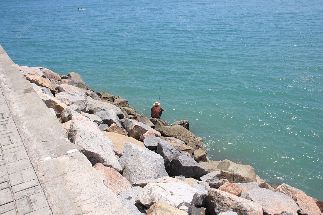 Homem sentado em rochas pescando no mar