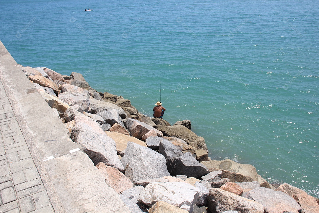 Homem sentado em rochas pescando no mar
