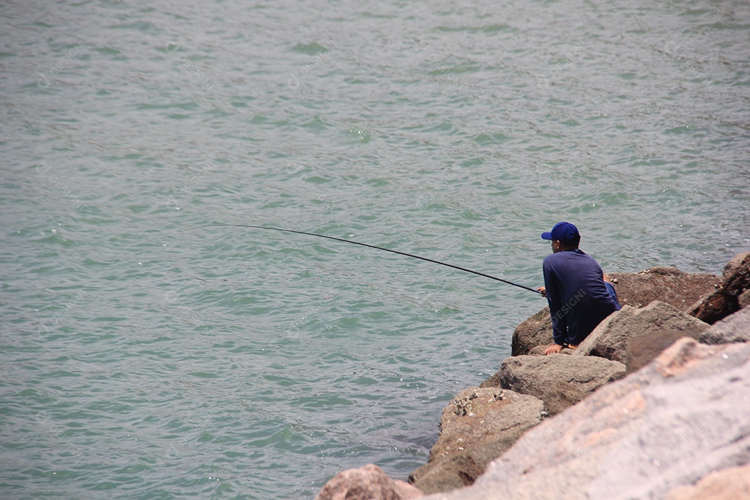 Homem sentado em rochas pescando no mar