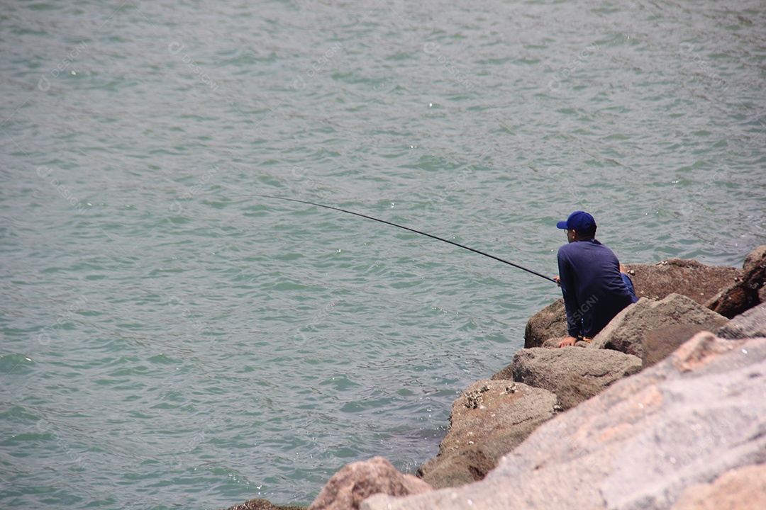 Homem sentado em rochas pescando no mar