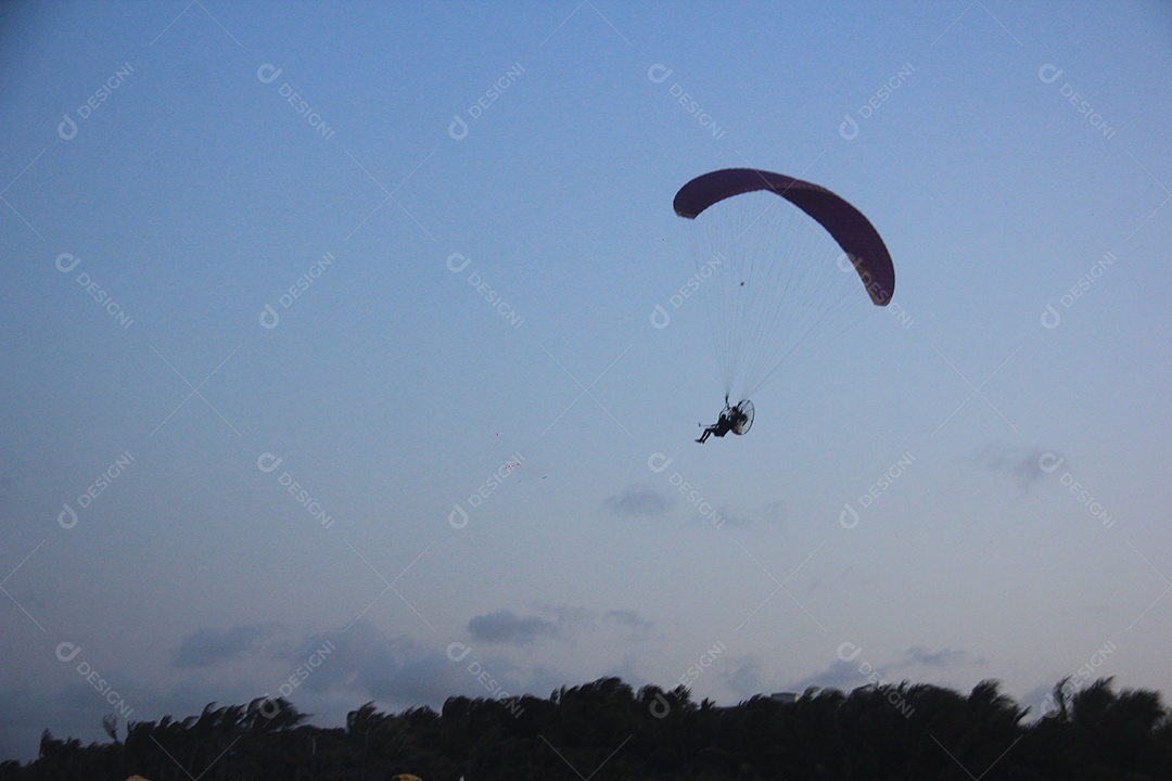 Silhueta, paraquedista usando um paramotor sobre o mar ao entardecer