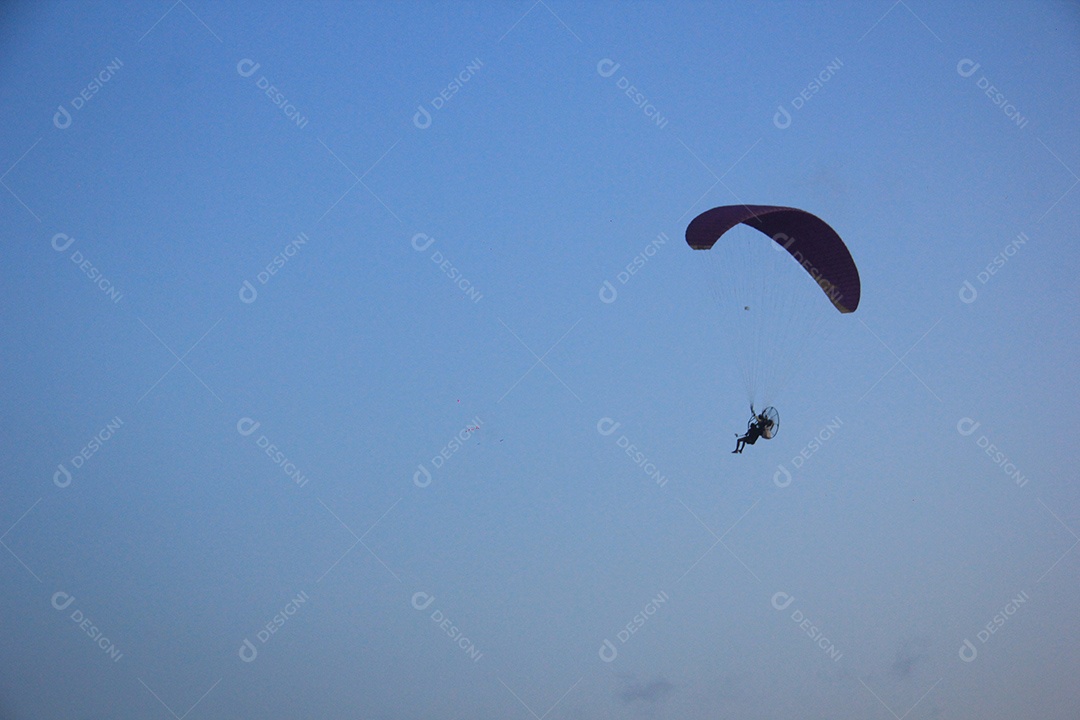Silhueta, paraquedista usando um paramotor sobre o mar ao entardecer