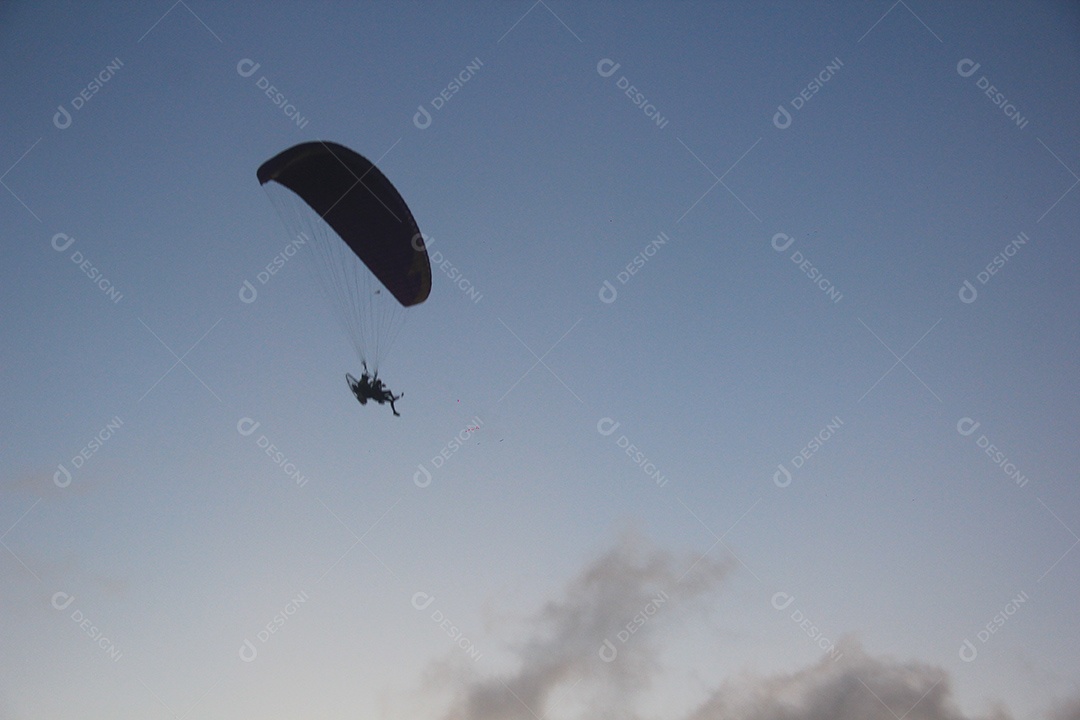 Silhueta, paraquedista usando um paramotor sobre o mar ao entardecer
