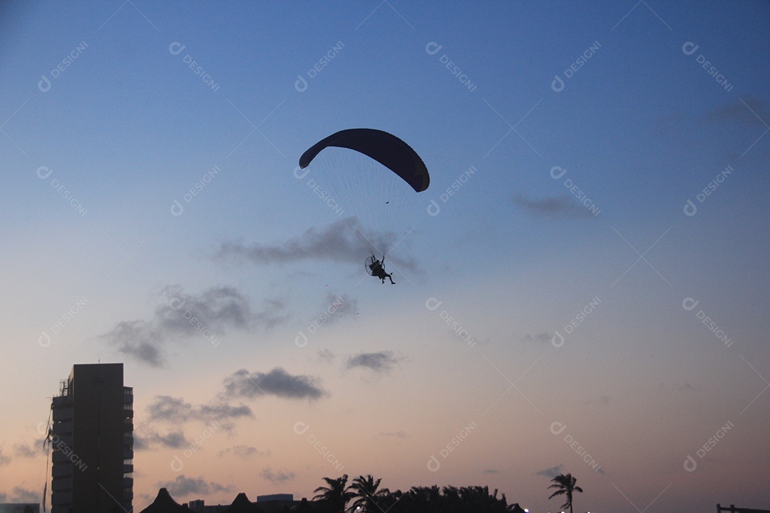 Silhueta, paraquedista usando um paramotor sobre o mar ao entardecer