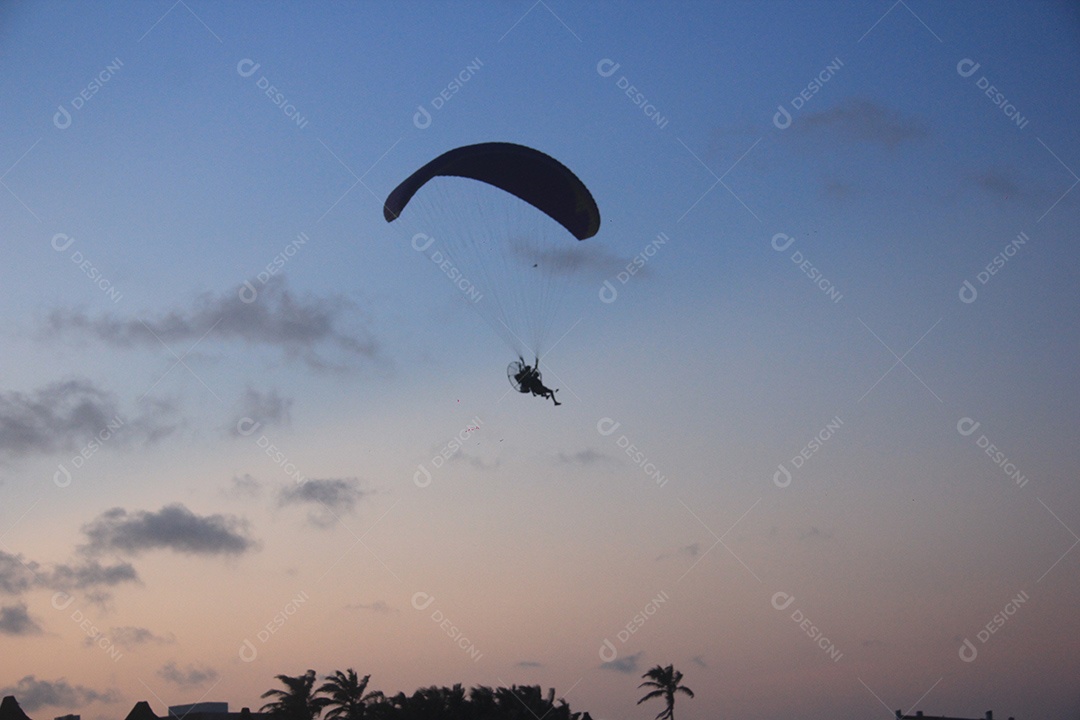 Silhueta, paraquedista usando um paramotor sobre o mar ao entardecer