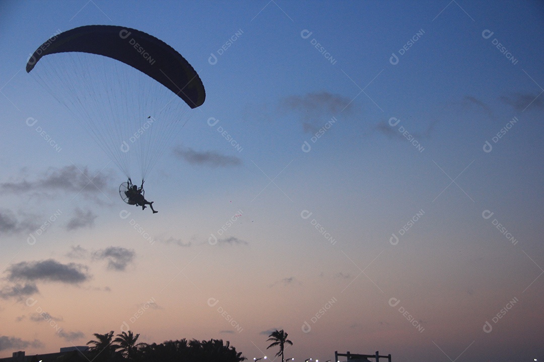 Silhueta, paraquedista usando um paramotor sobre o mar ao entardecer