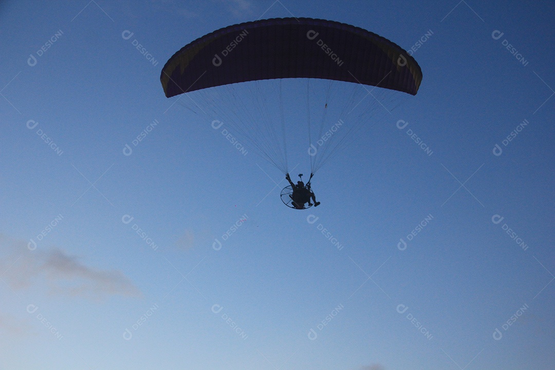 Silhueta, paraquedista usando um paramotor sobre o mar ao entardecer