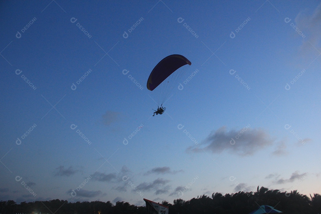 Silhueta, paraquedista usando um paramotor sobre o mar ao entardecer