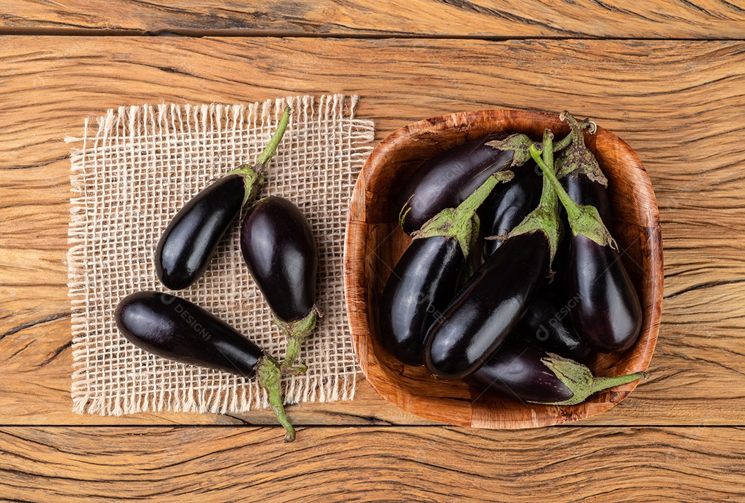 Berinjelas de bebê minúsculo em uma tigela sobre a mesa de madeira.