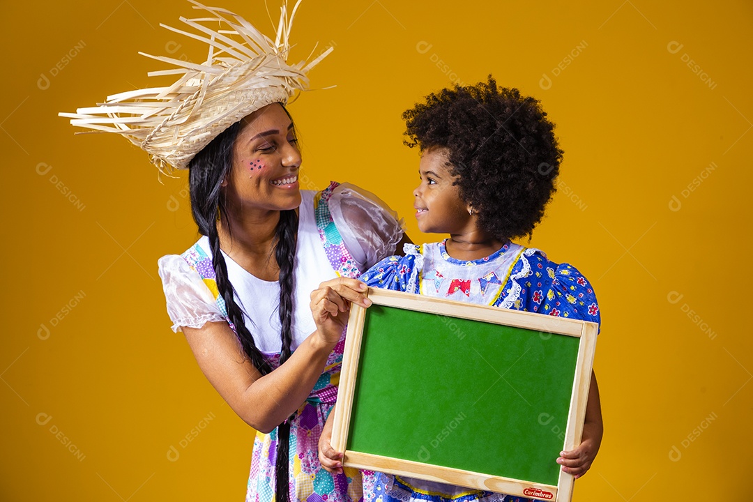 Mulher jovem com sua filha segurando quadro negro fantasiadas São João