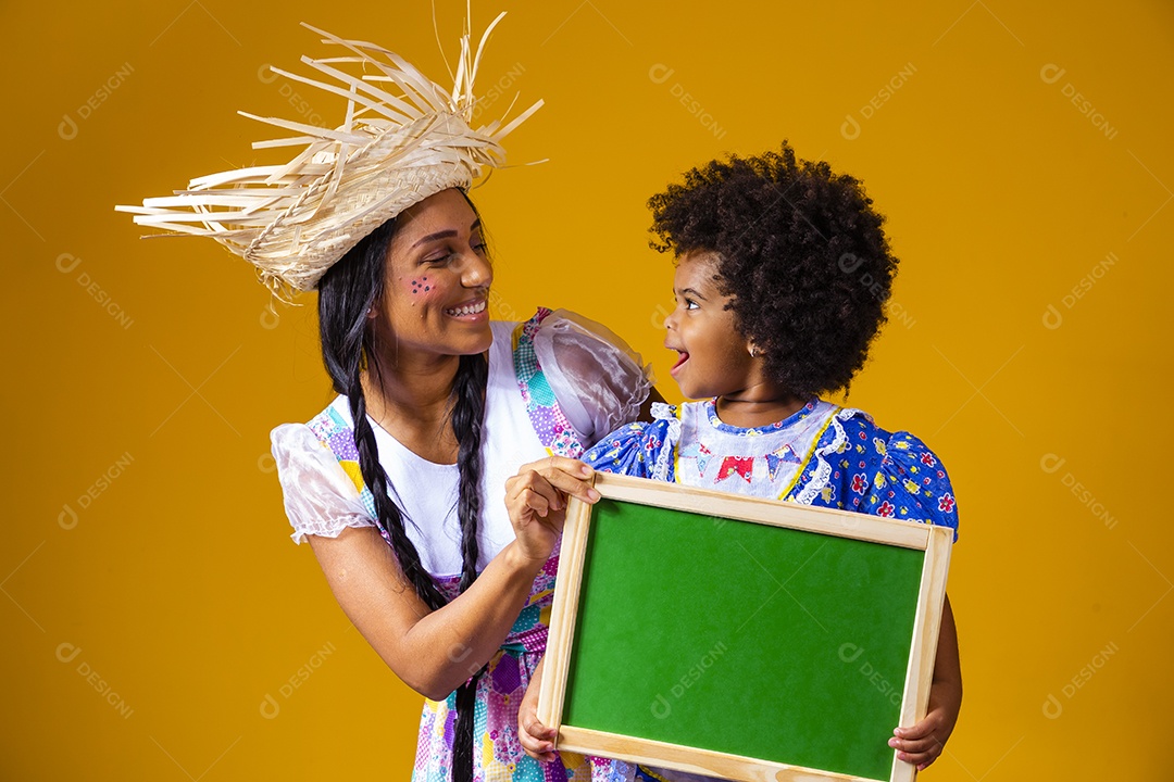 Mulher jovem com sua filha segurando quadro negro fantasiadas São João