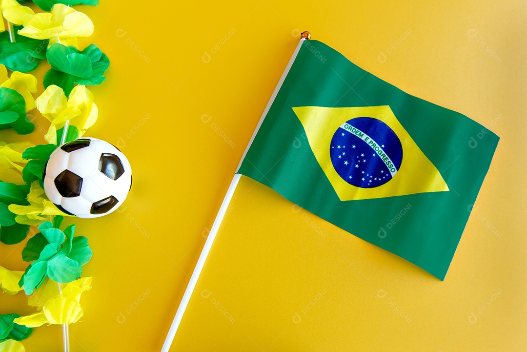 Bola de futebol e bandeira brasileira em fundo amarelo.