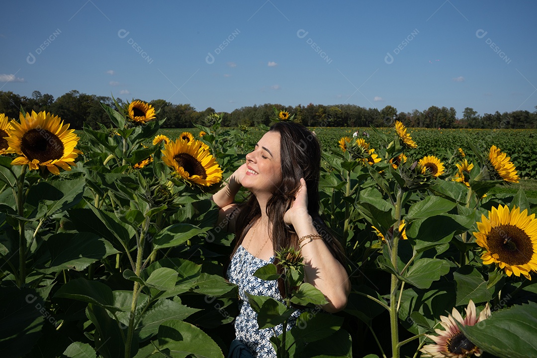 Mulher sorrindo e sentindo o sol em uma plantação de girassol.