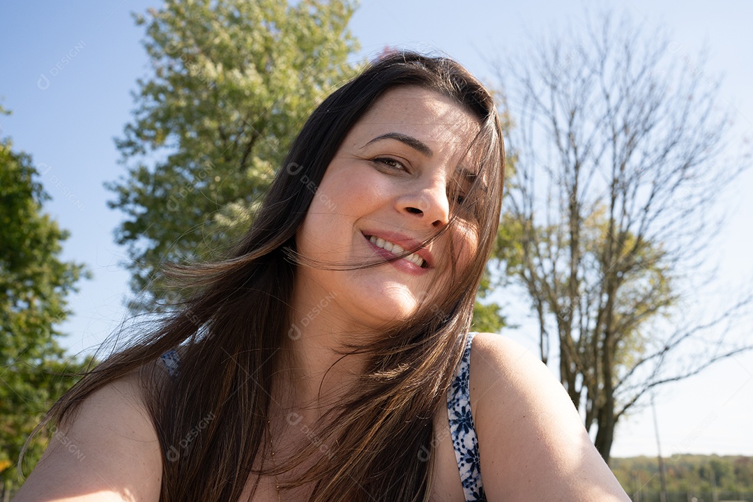 Mulher morena sorrindo em dia ensolarado.