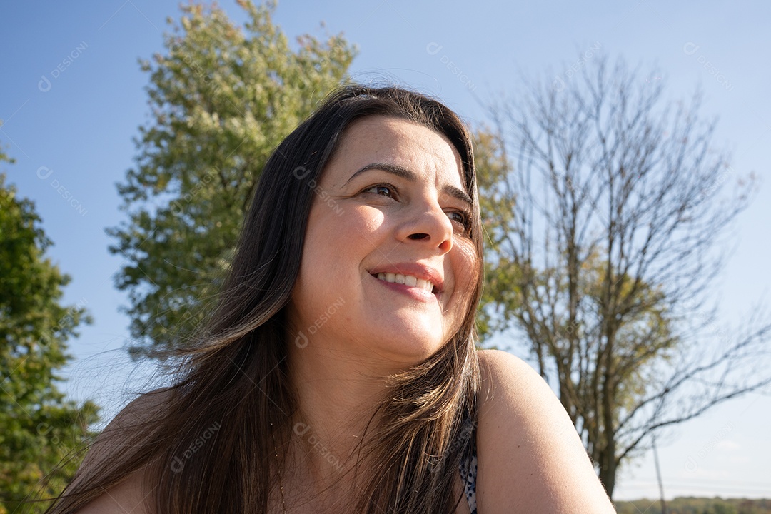 Mulher morena sorrindo em dia ensolarado.