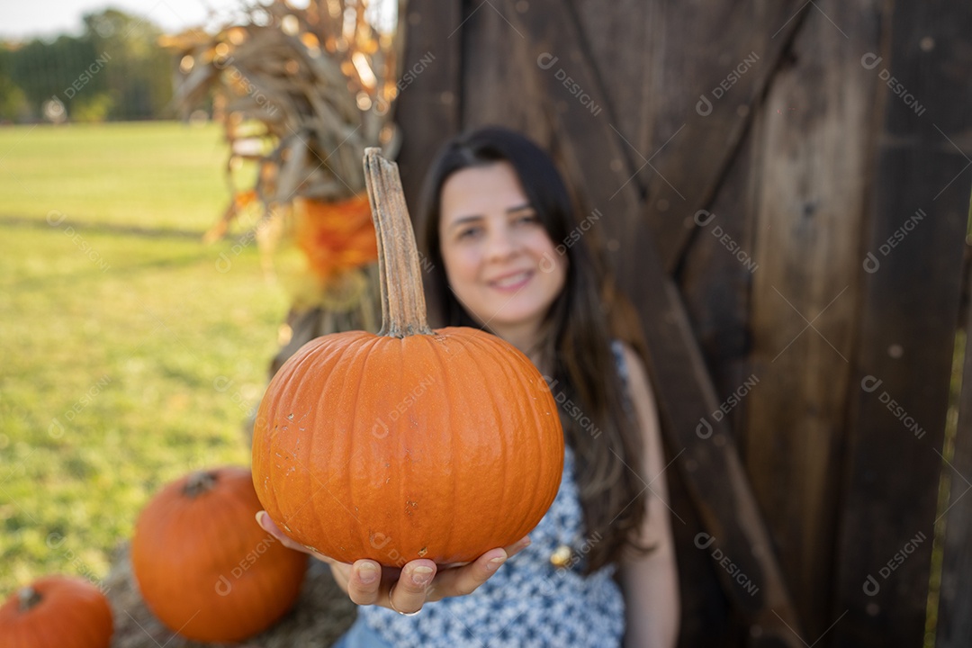 Mulher sorrindo com rosto borrado e segurando abóbora na fazenda.