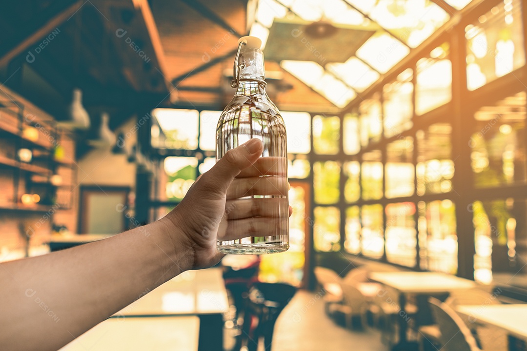 Mão segurando uma garrafa de vidro de água no café.