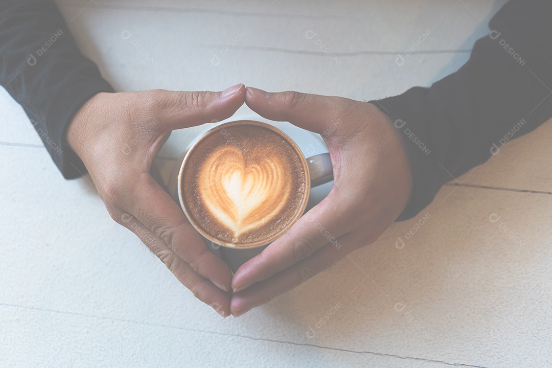Mão segurando a xícara de café cappuccino na mesa branca no estilo de vida moderno vintage do conceito de cafeteria.