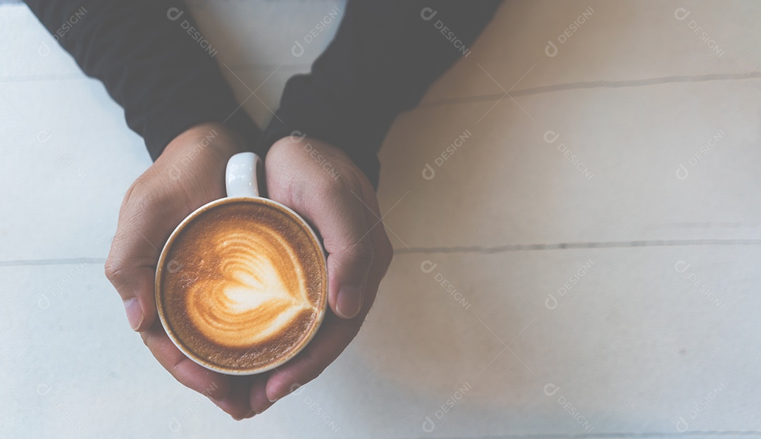 Mão segurando a xícara de café cappuccino na mesa branca no estilo de vida moderno vintage do conceito de cafeteria.