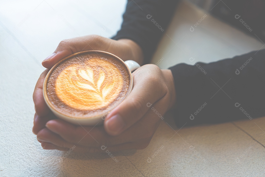Mão segurando a xícara de café cappuccino na mesa branca no estilo de vida moderno vintage do conceito de cafeteria.
