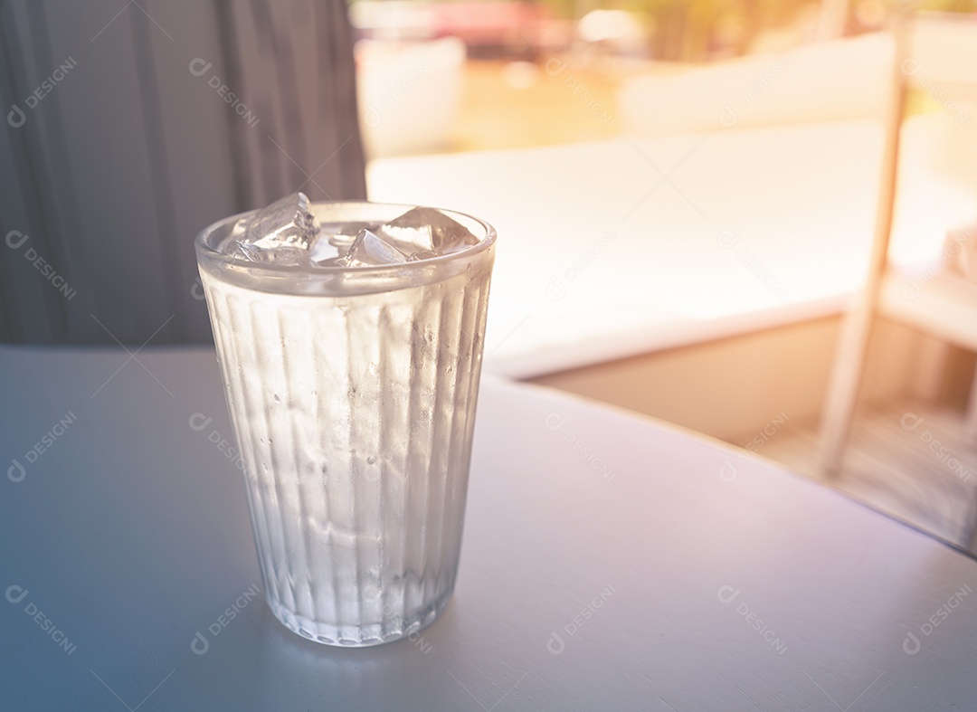 Água fresca com gelo no copo na mesa branca.