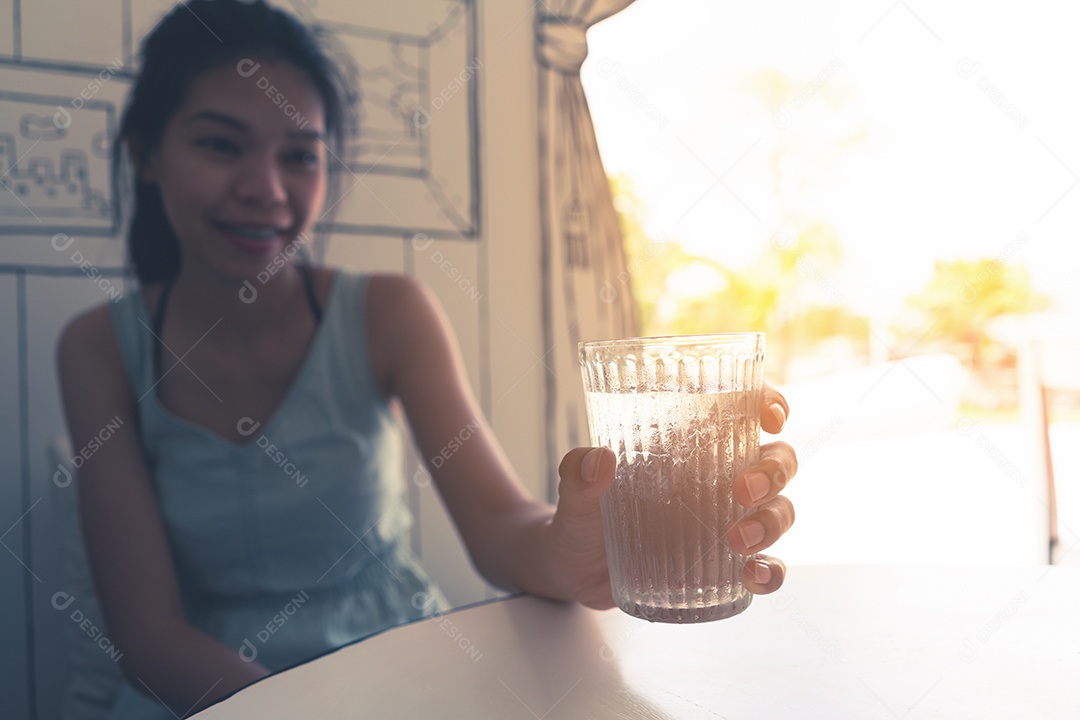 Mão segurando água fresca com gelo no copo na mesa branca.