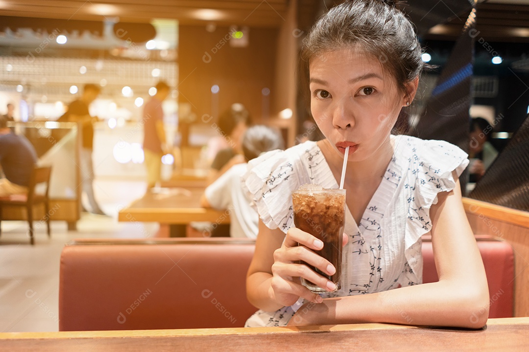 Garota segurando água fresca de cola com gelo no copo na loja de comida.