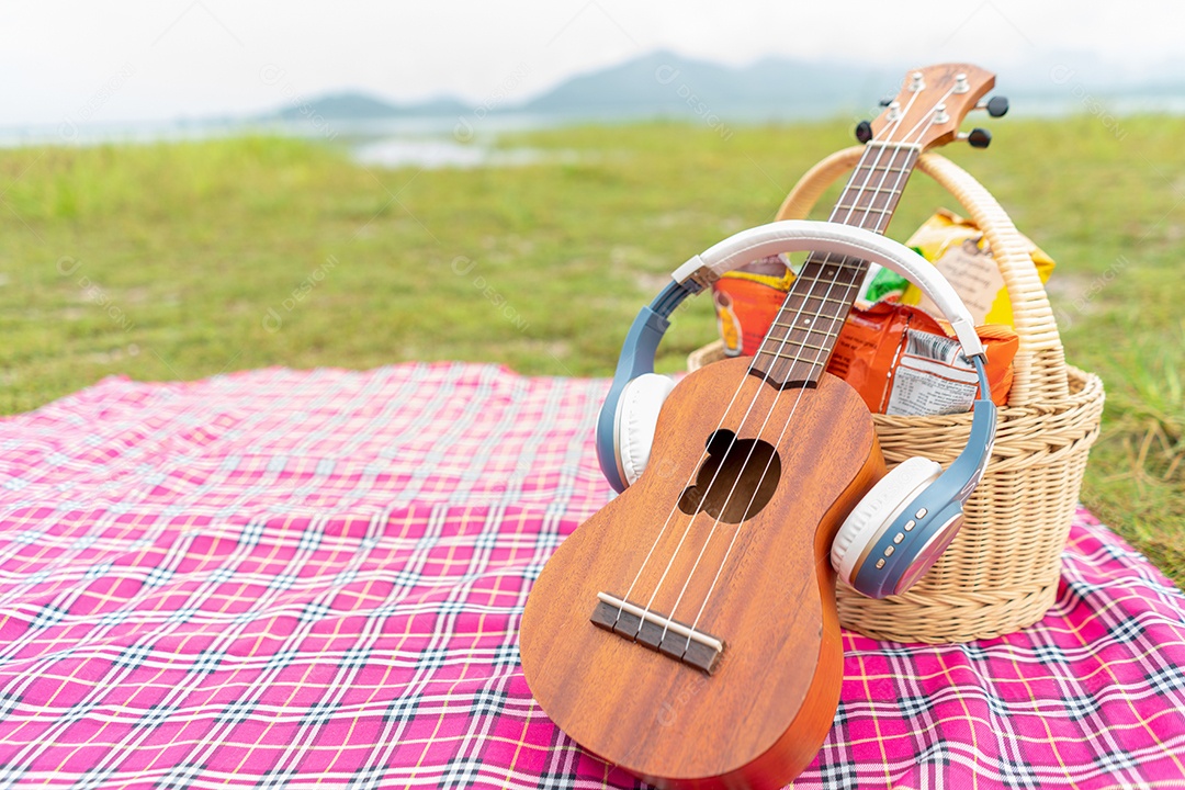 Ukulele sobre som de ouvido e comida no cobertor de linho de piquenique no jardim para segundo plano.