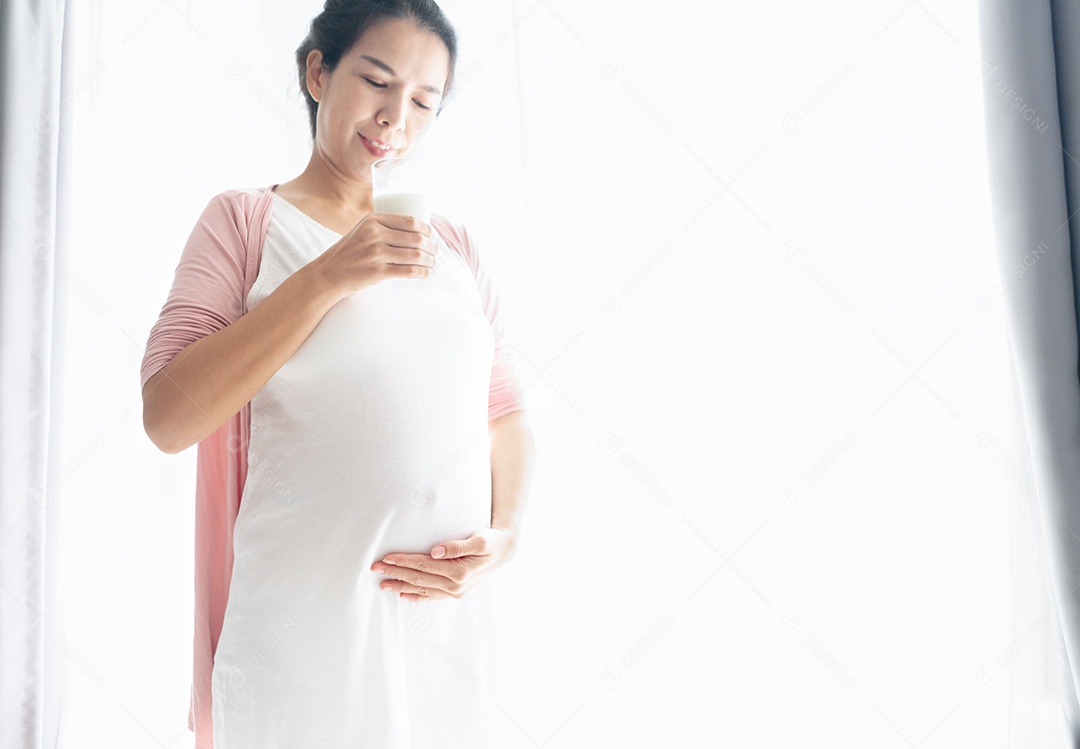Mulher grávida tocando a barriga e segurando um copo de leite.