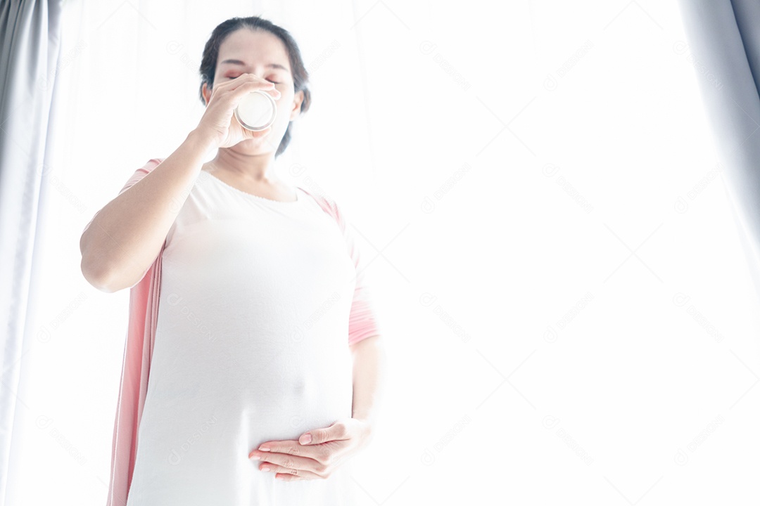 Mulher grávida tocando a barriga e segurando um copo de leite.