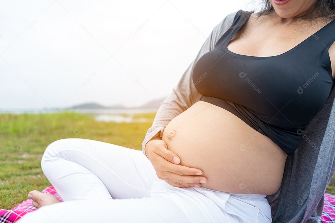 Mulher grávida tocando a barriga no jardim por amor e expectativa.