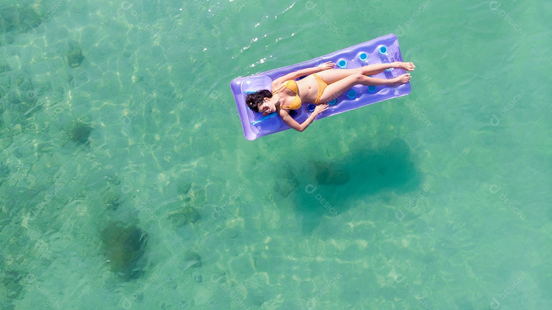 A mulher asiática relaxa tomando sol no sofá de ar.