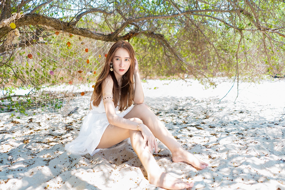 A bela viajante asiática de vestido branco relaxa na praia.